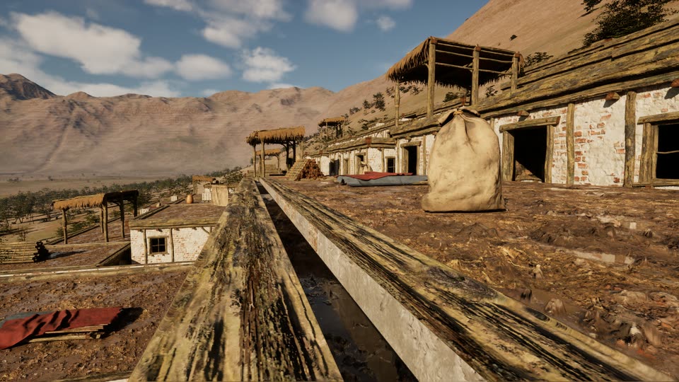Across flat earth roofs edged with timber beams: whitewashed walls, reed-roofed shade frames, a grain sack and bedding on a roof, and dry mountains in the distance.